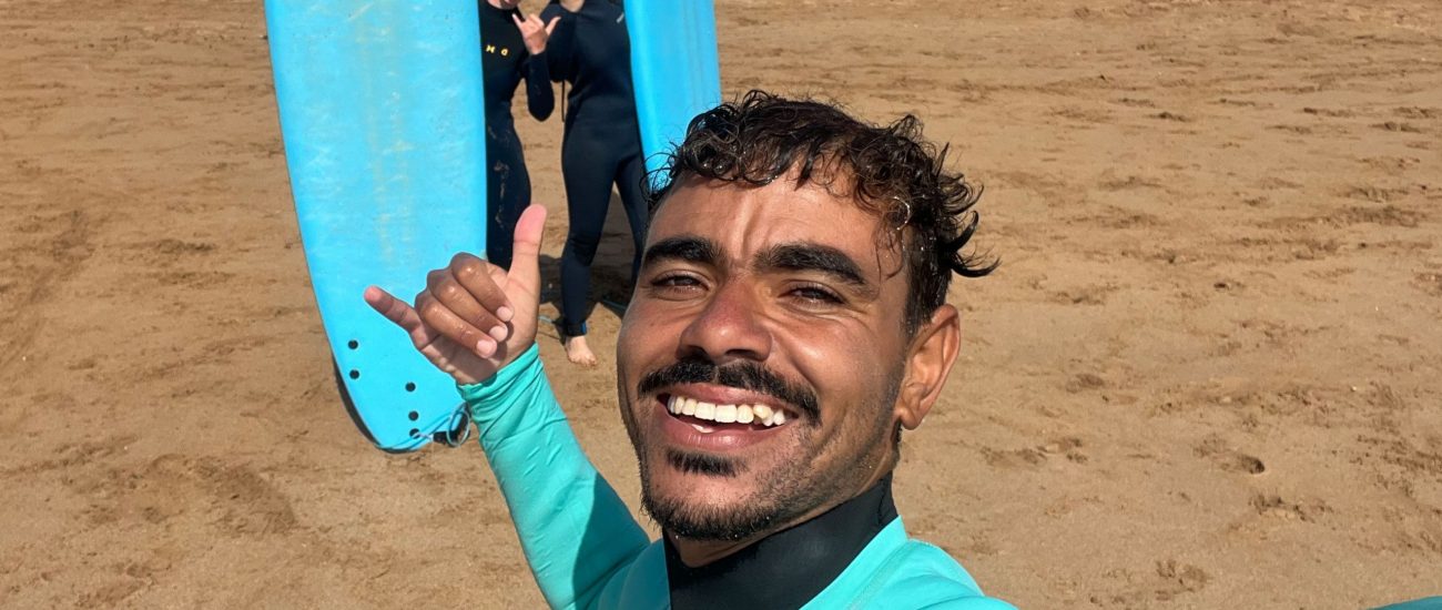 Momo and two girls smiling holding their surf boards at the beach of Sidi Kaouki after finishing a surf lesson