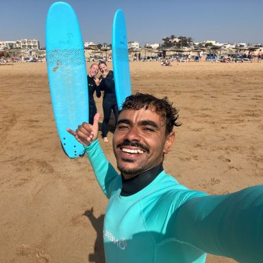 Momo and two girls smiling holding their surf boards at the beach of Sidi Kaouki after finishing a surf lesson