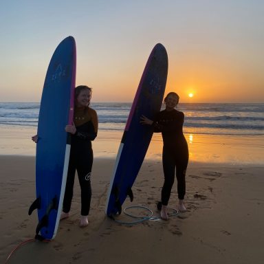 Two girls standing on the beach of Sidi Kaouki during sunset with their surf boards smiling