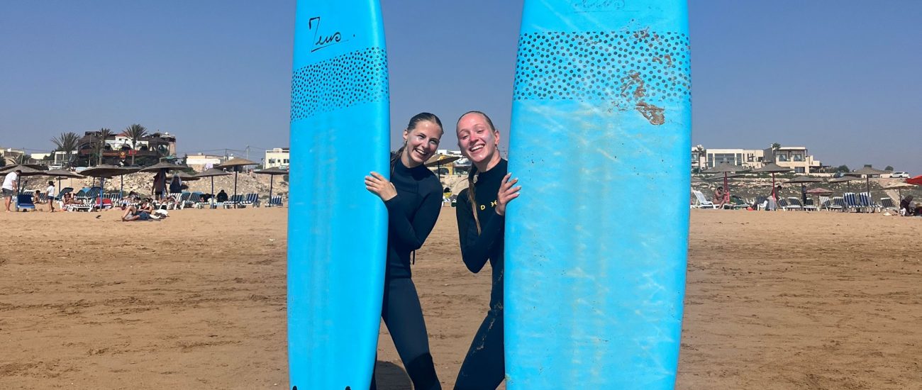 Two girls standing on the beach of Sidi Kaouki with their surf boards smiling