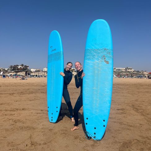 Two girls standing on the beach of Sidi Kaouki with their surf boards smiling