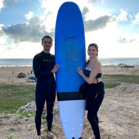 a couple standing beside a surf board smiling in Sidi Kaouki