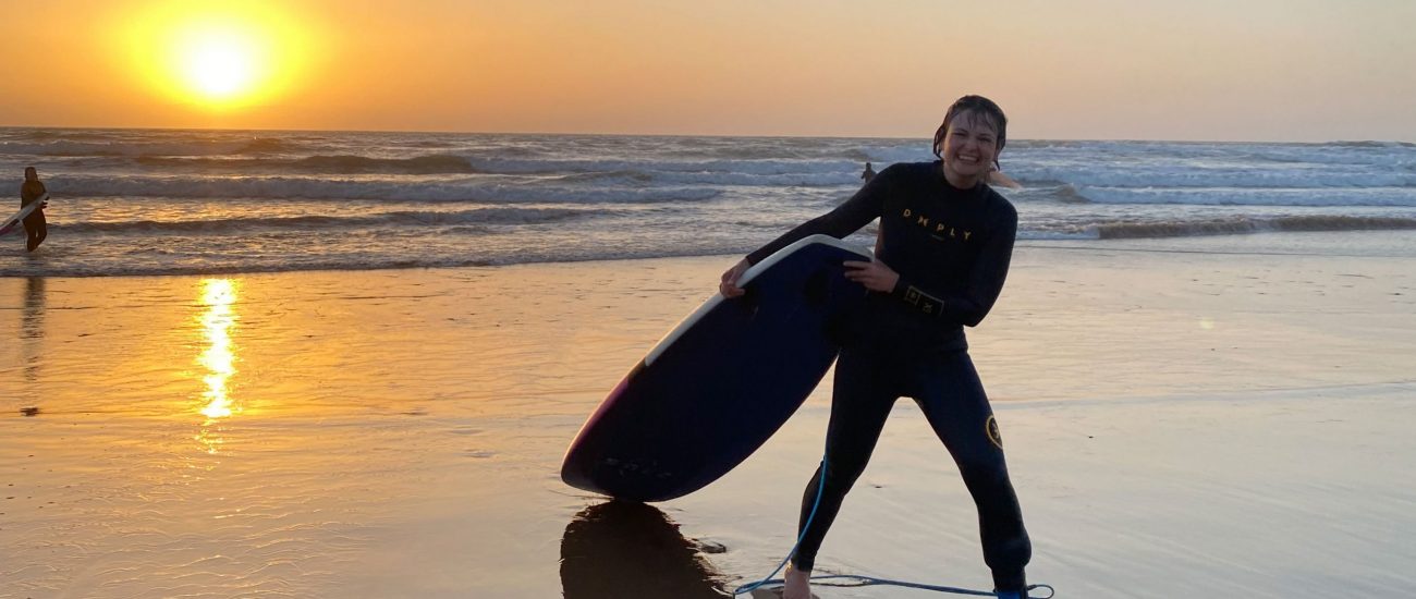 a girl coming out of the ocean with a surfboard while the sun is going down