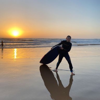 a girl coming out of the ocean with a surfboard while the sun is going down