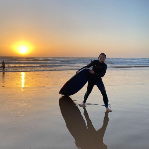 a girl coming out of the ocean with a surfboard while the sun is going down