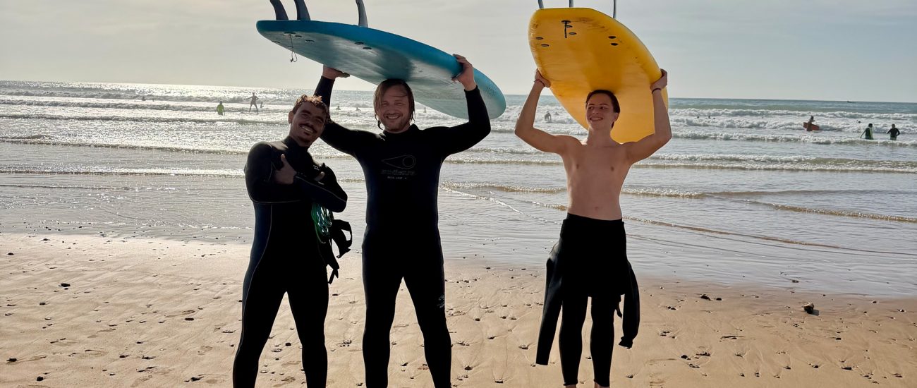 two-Guys taking a surf lesson lesson with Momo in Sidi Kaouki holding their boards beneath theri head