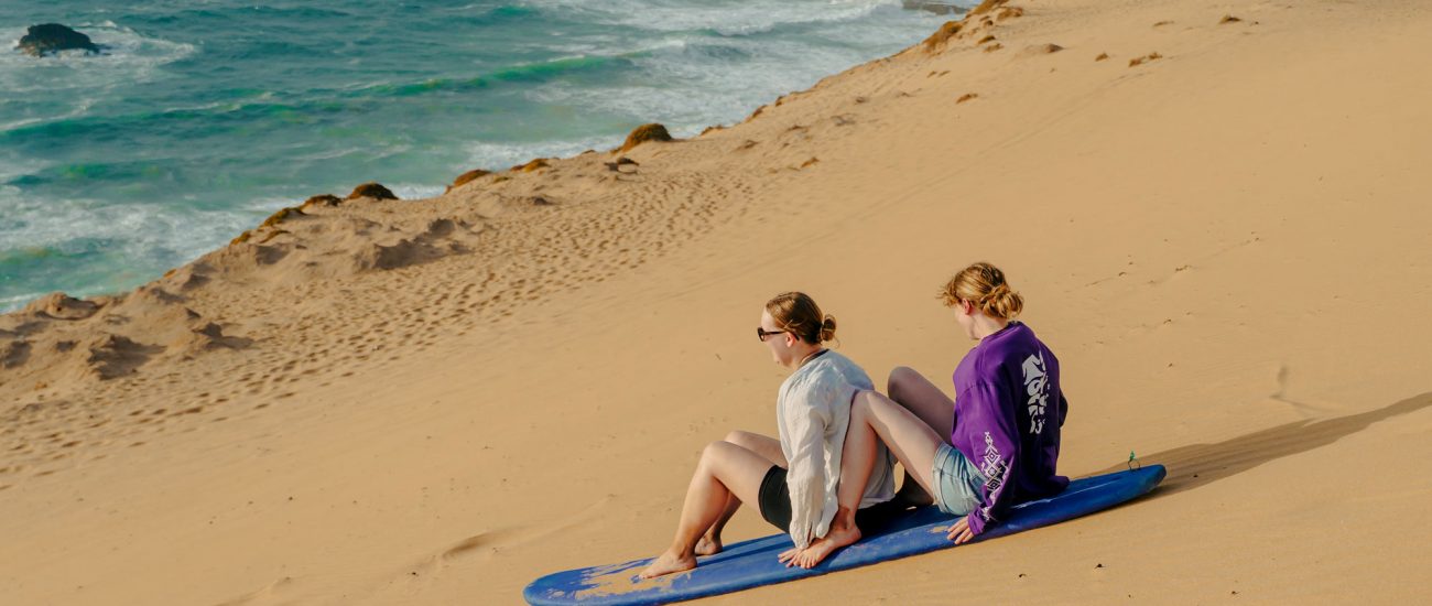 two woman sandboarding in Sidi Kaouki in the sand dunes beside the ocean
