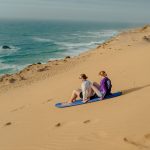 two woman sandboarding in Sidi Kaouki in the sand dunes beside the ocean