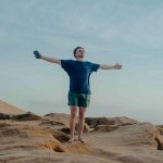 man standing ion a sand dunes in Sidi Kaouki lifting his arms up