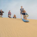 a group of people sandboarding in Sidi Kaouki in the sand dunes