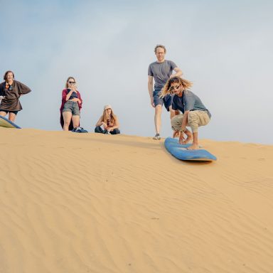a group of people sandboarding in Sidi Kaouki in the sand dunes